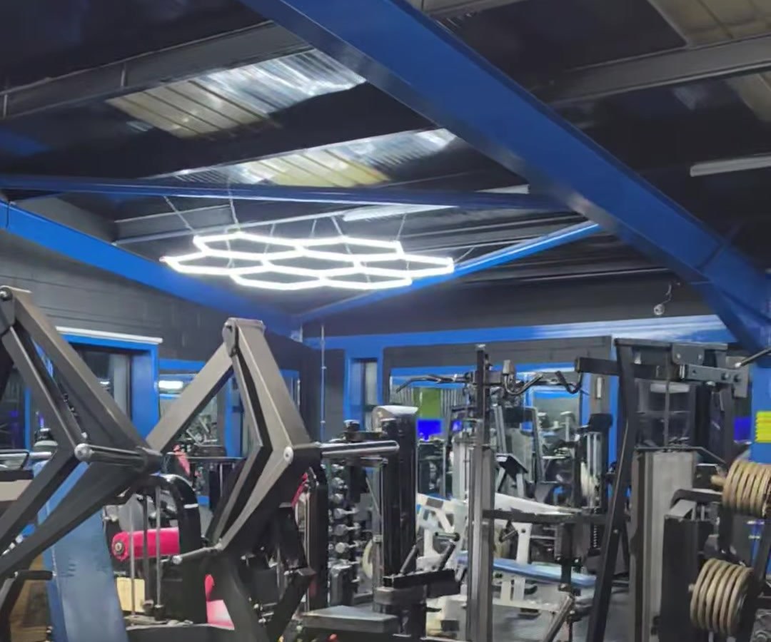 The RAW gym floor: rows of plate-loaded machines under a white hexagon LED light and blue steel beams