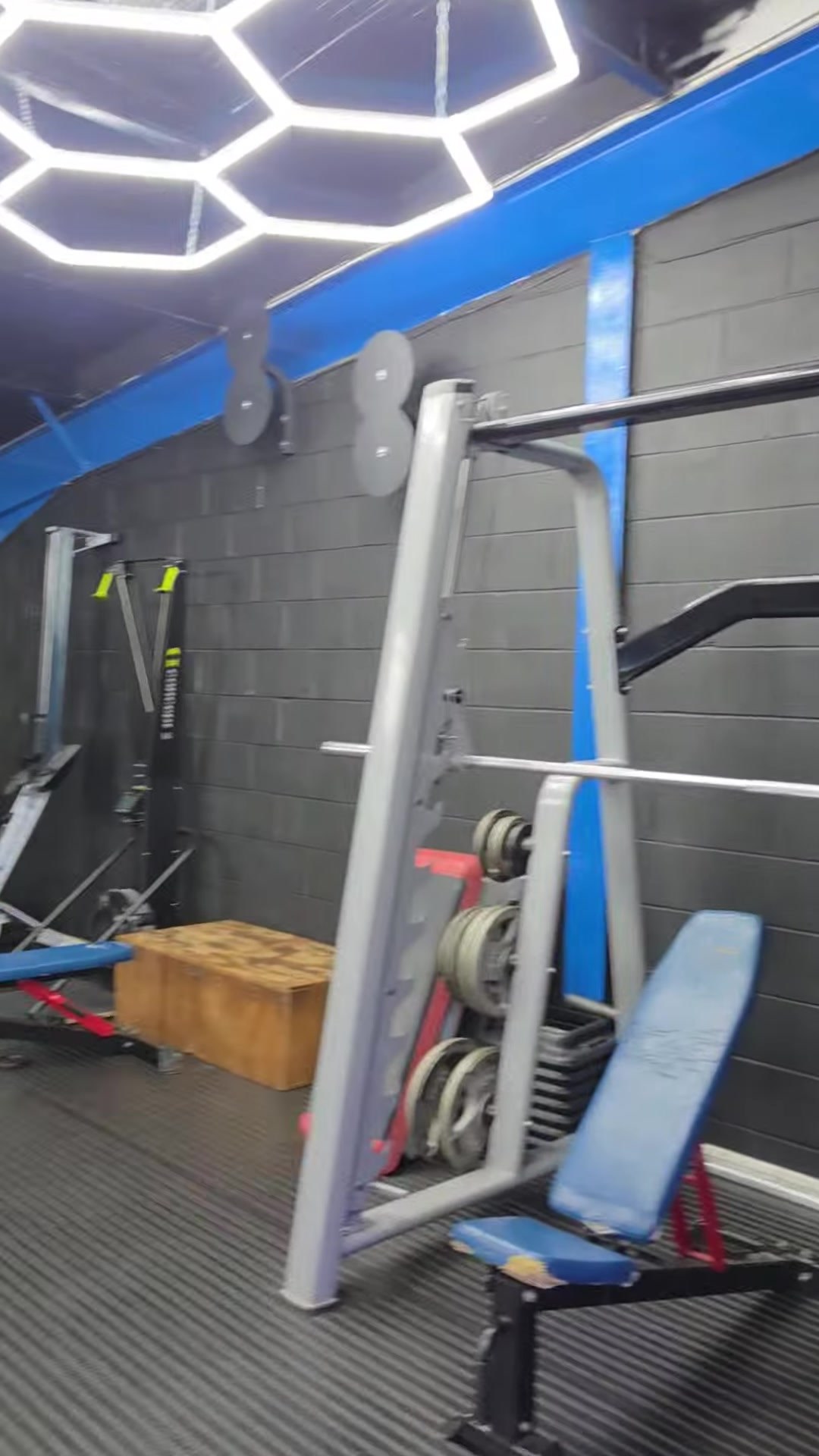 Smith machine, bench and plyo box beneath the hexagon LED lights against black block walls